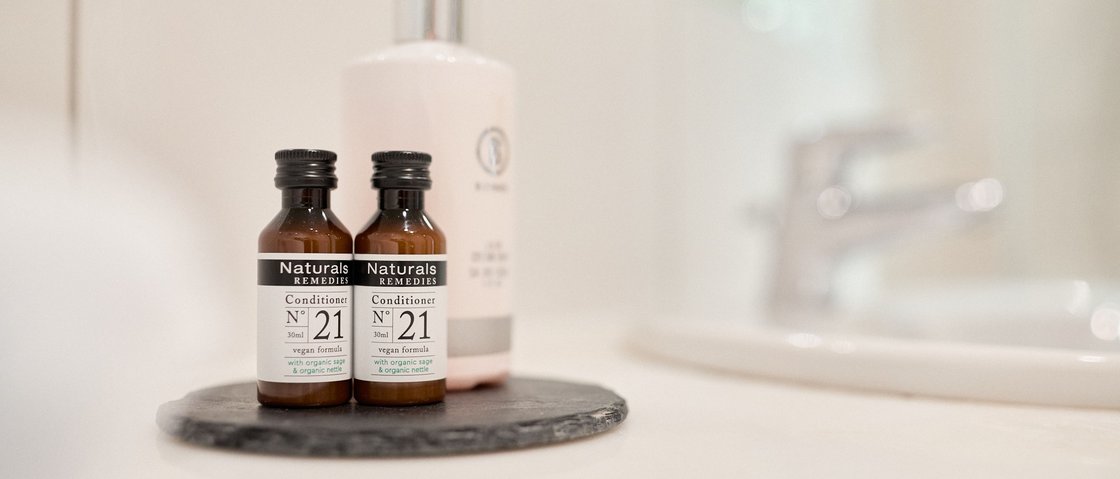 Entspannen im Wellnesshotel im Stubaital Zwei kleine Naturkosmetik Conditioner Flaschen auf einem schwarzen Untersetzer im Badezimmer