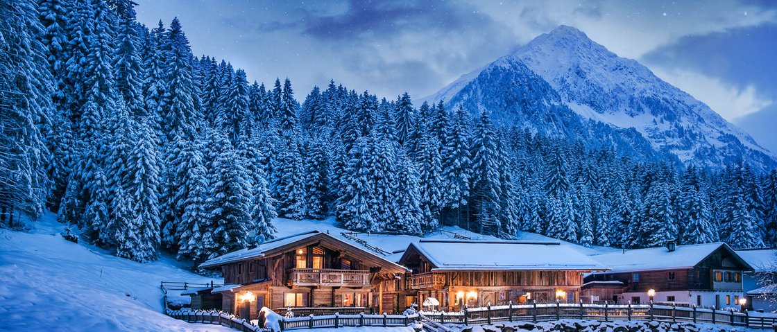 Sich erholen im Hotel in Neustift im Stubaital Winterlandschaft mit beleuchteten Holzhäusern und schneebedeckten Bergen