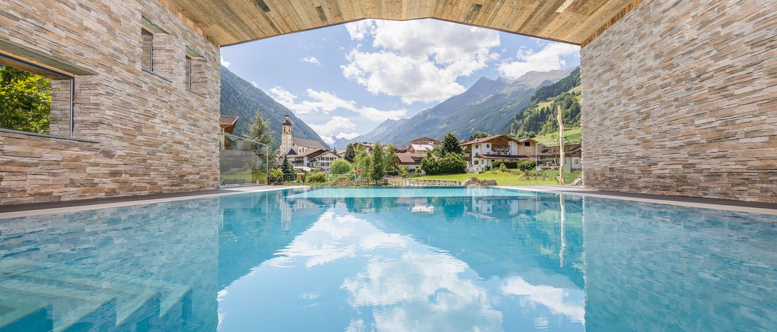 Sich erholen im Hotel in Neustift im Stubaital Überdachter Pool mit Blick auf Alpen, Häuser und blauen Himmel mit Wolken