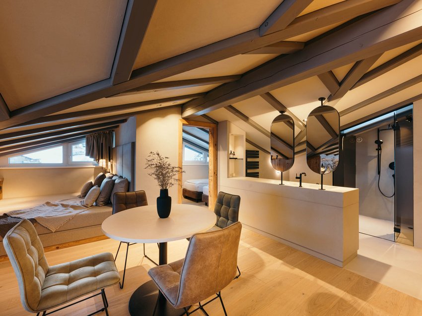 Sich erholen im Hotel in Neustift im Stubaital Gemütliches Dachzimmer mit Bett, Tisch, Stühlen und Badezimmer mit Spiegeln