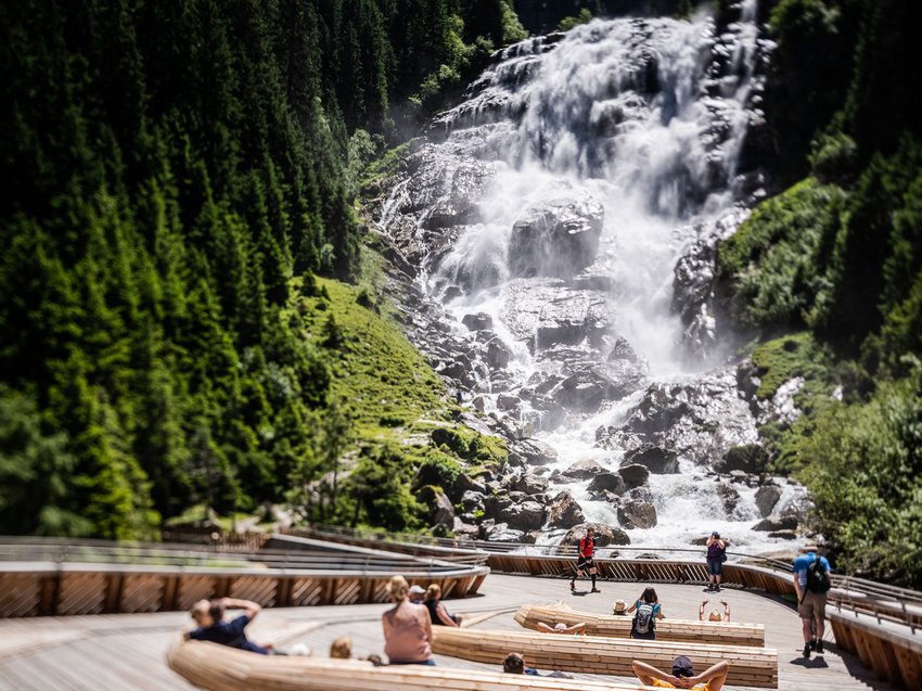Sich erholen im Hotel in Neustift im Stubaital Besucher sitzen und laufen vor einem großen Wasserfall in einem bewaldeten Tal
