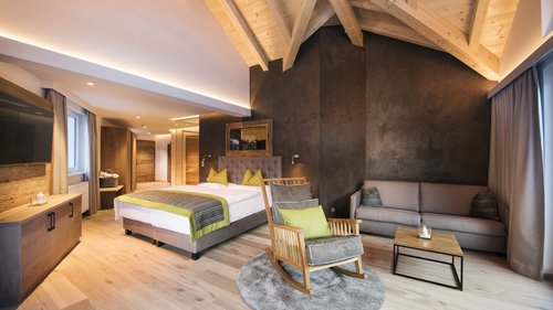 Sich erholen im Hotel in Neustift im Stubaital Modernes Hotelzimmer mit Holzmöbeln, einem Bett, Schaukelstuhl und Sofa
