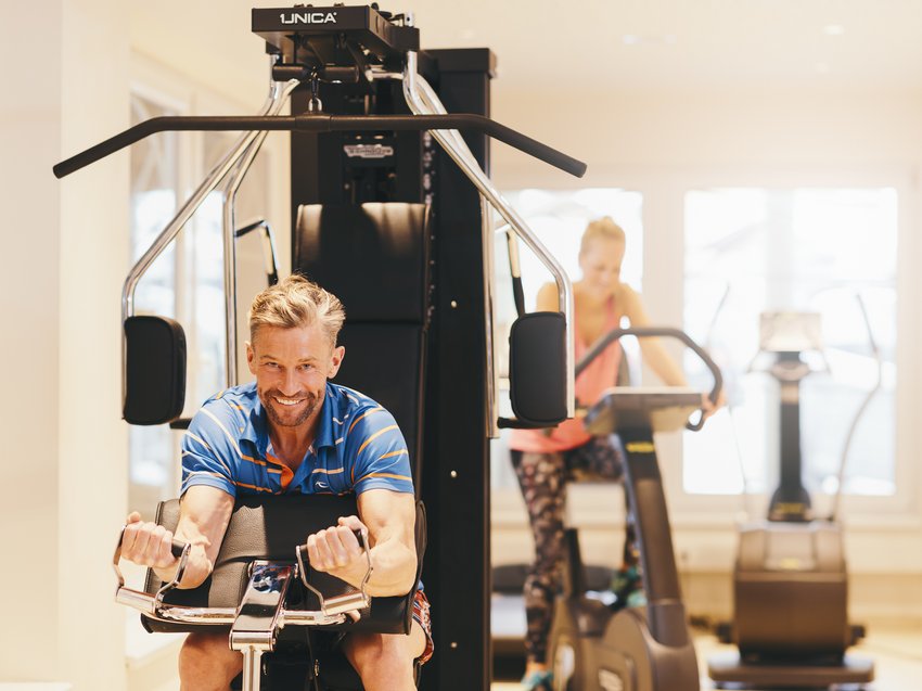 Entspannen im Wellnesshotel im Stubaital Mann trainiert mit Fitnessgerät, Frau fährt im Hintergrund Fahrrad im Fitnessraum