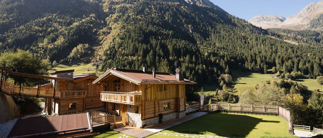 Sich erholen im Hotel in Neustift im Stubaital Holzhütten mit Bergkulisse und Grünflächen an sonnigem Tag