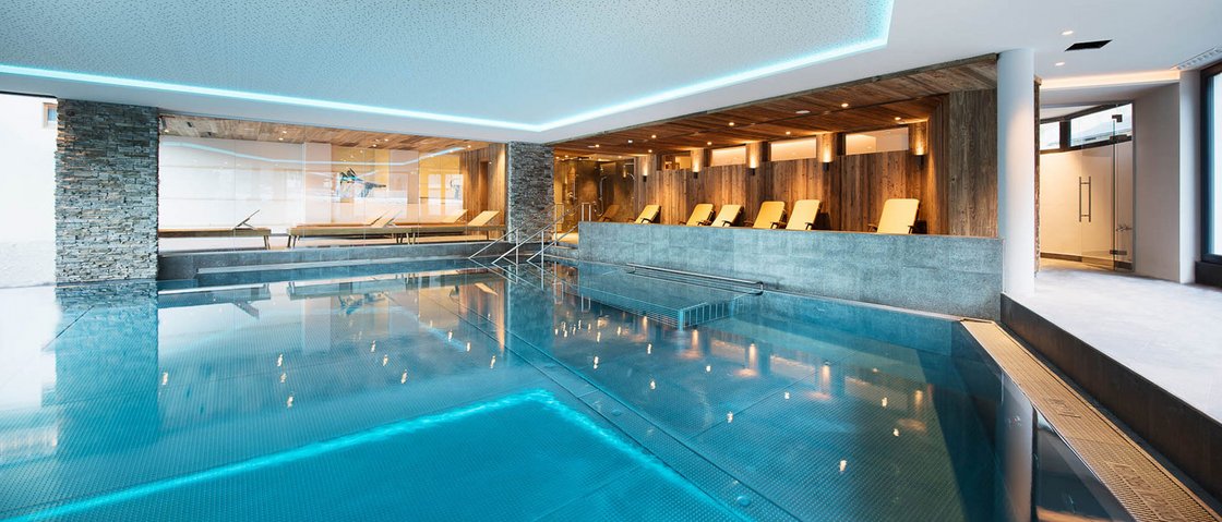 Entspannen im Wellnesshotel im Stubaital Moderner Innenpool mit Liegestühlen und Holzverkleidung an der Wand