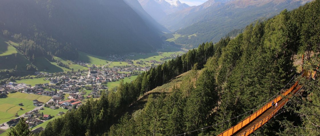 Ready for your holiday in Stubaital this summer? Suspension bridge over forest with mountain valley and village in background